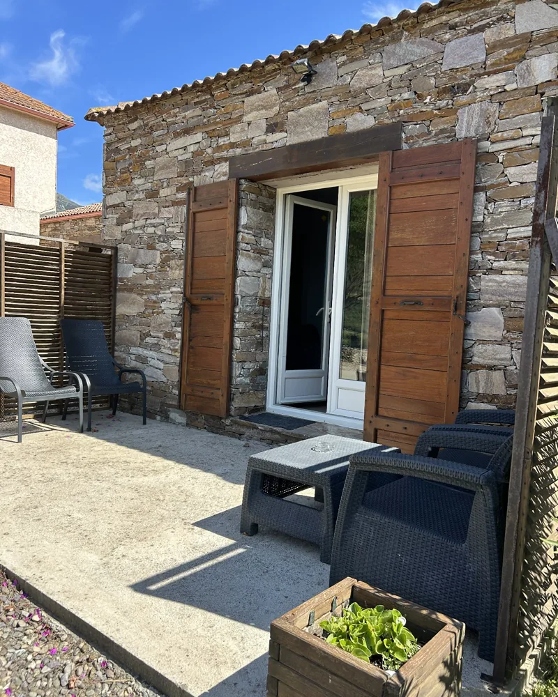 Terrasse privée de la suite devant sa façade en pierre, avec salon de jardin